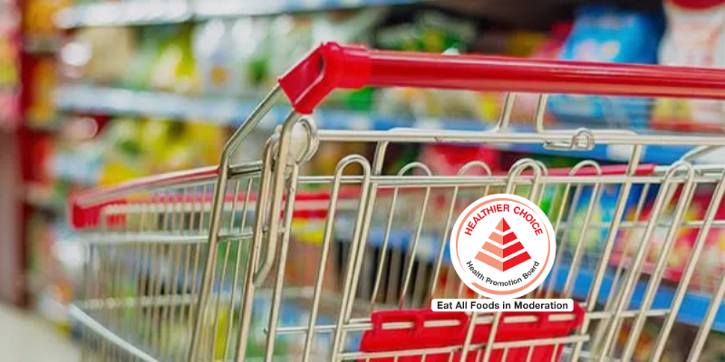 Close-up of a shopping cart in a supermarket aisle with shelves of products in the background.